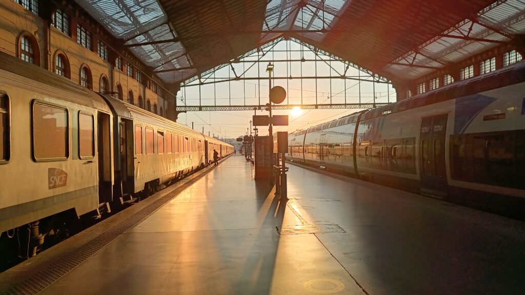 Quai de la gare Marseille St-Charles au petit matin, alors que le soleil rasant illumine la rame Corail et l'AGC à quai